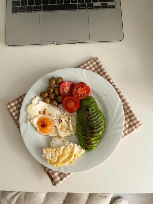 This image depicts a nutritious meal featuring one medium-cooked egg accompanied by diced tomatoes, garnished with herbs, and sliced avocado