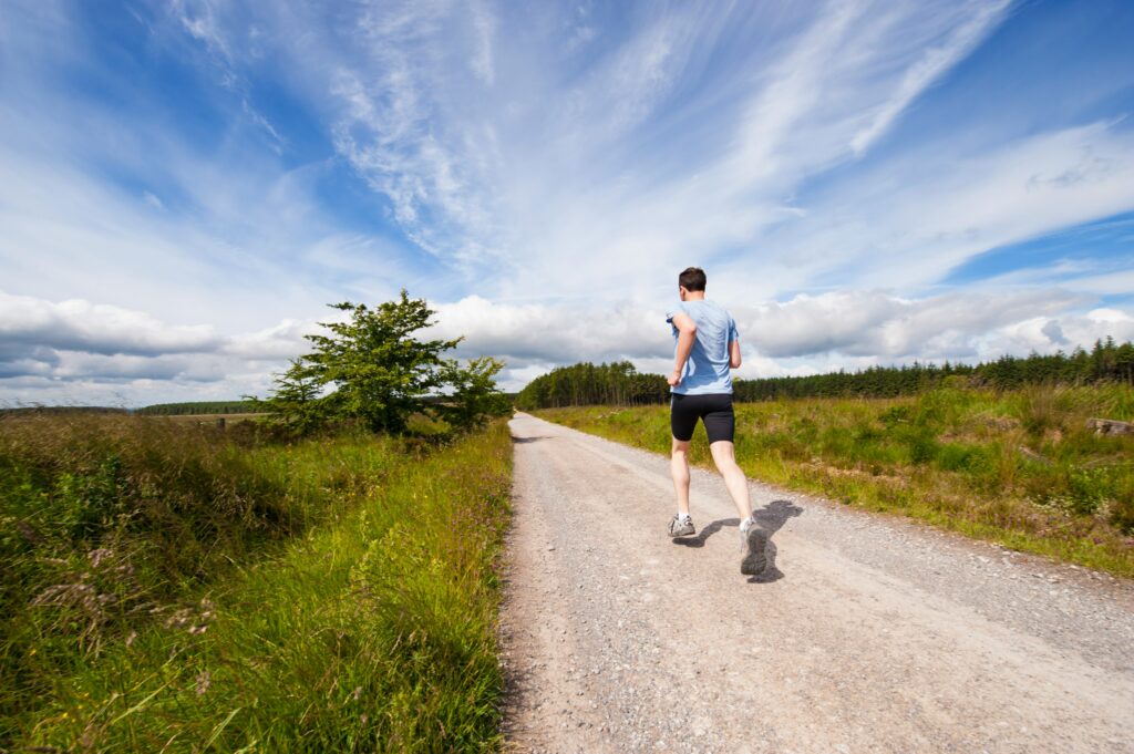 The photograph captures a male individual running on a road located in a park, heading away from the camera