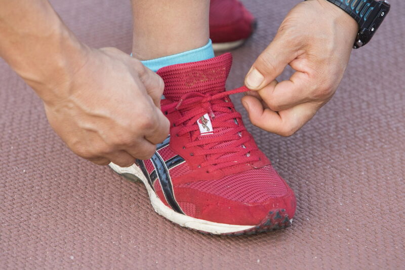 The photograph illustrates hands engaged in the process of lacing a red sneaker