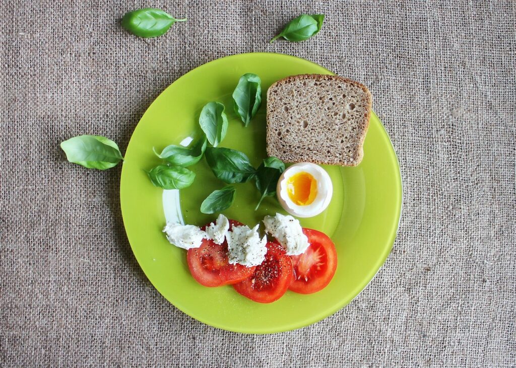 A healthy plate with slices of wheat bread, fresh tomato, a boiled egg, and assorted greens
