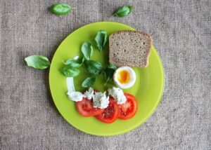 A healthy plate with slices of wheat bread, fresh tomato, a boiled egg, and assorted greens