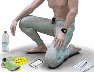 Half view of a man kneeling on his left knee without a shirt, wearing a digital watchband. On the floor around him are a water bottle, mobile phone, wireless earphones, a running logbook with a pen on top, and a pair of sneakers.