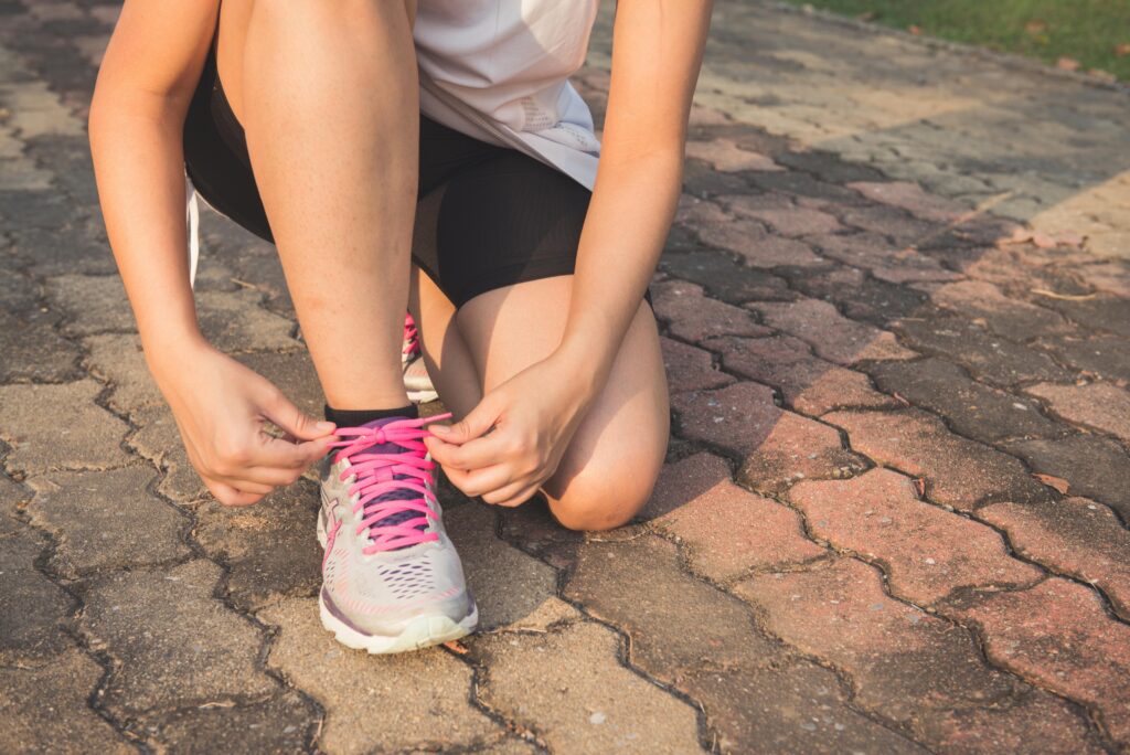 Close-up of a person tying the laces on their running shoes, preparing for a workout on a sunny outdoor path