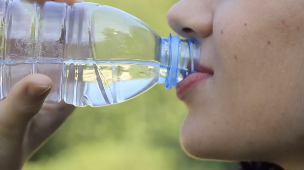Close-up of a woman drinking from a water bottle, showing only her nose, lips, and chin.